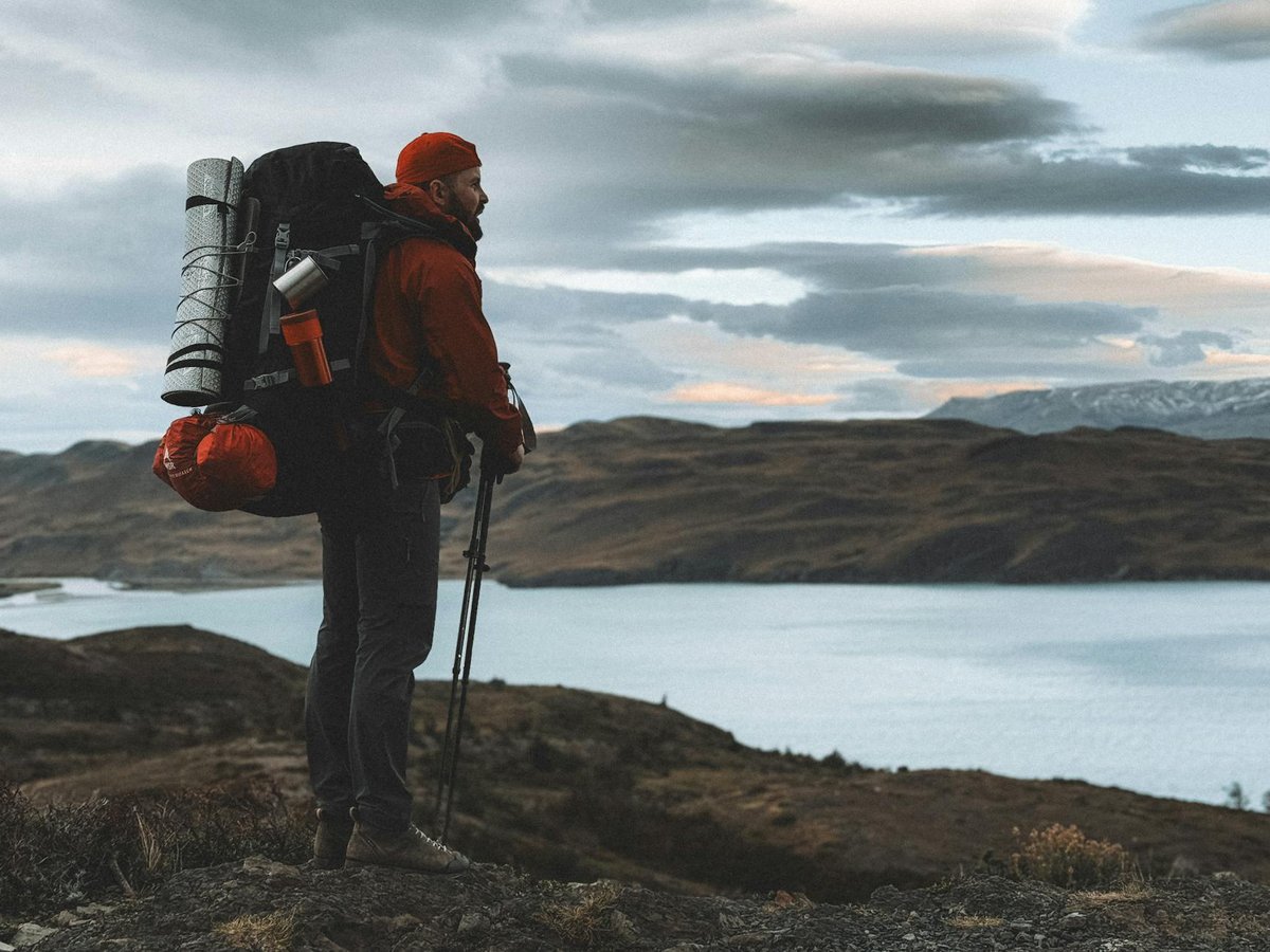 Solo hiker with backpack standing on hillside overlooking turquoise lake in Patagonian landscape