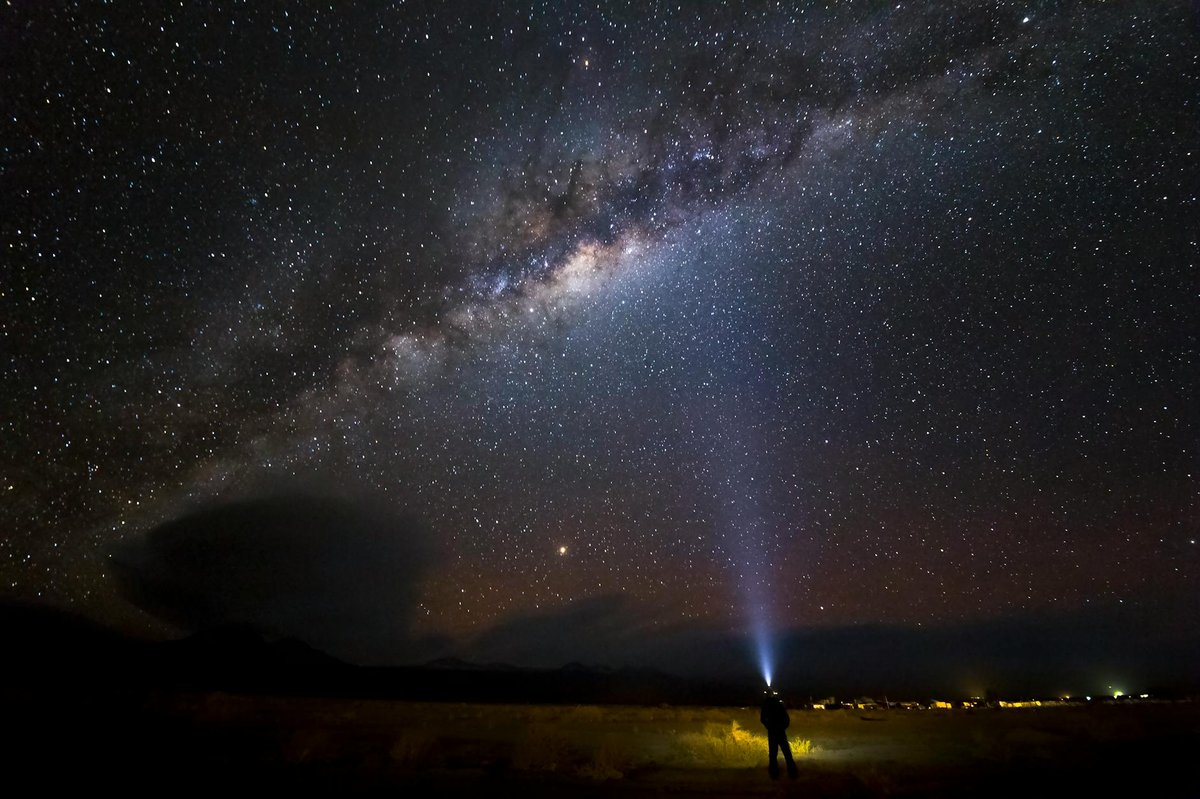 Person standing under the Milky Way in the Atacama Desert with flashlight pointing at star-filled sky