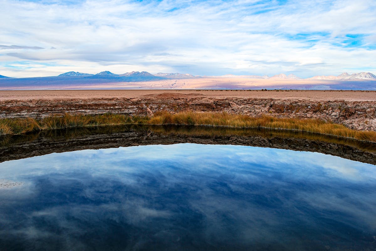 Serene clear-water lagoon in the Atacama Desert with mountain reflections under blue sky