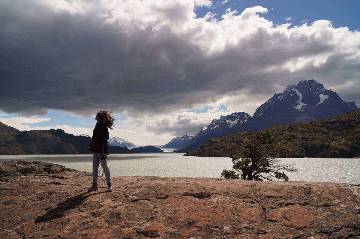 Hiker standing on rock overlooking Torres del Paine landscape with dramatic clouds