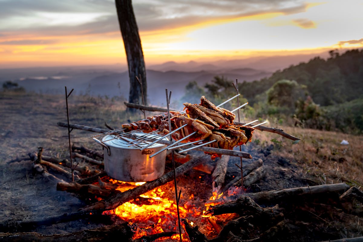 Outdoor cooking setup over a campfire with pots and grill