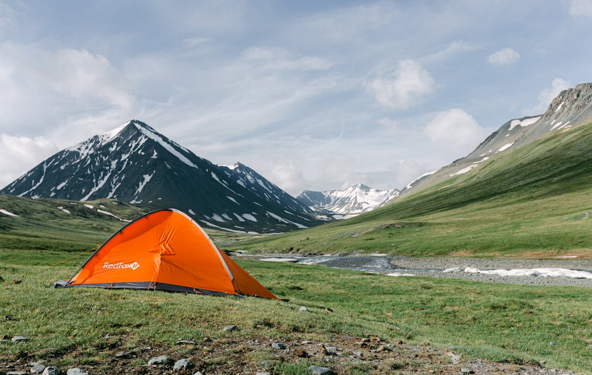 Tent set up in a remote mountain valley beside a flowing river