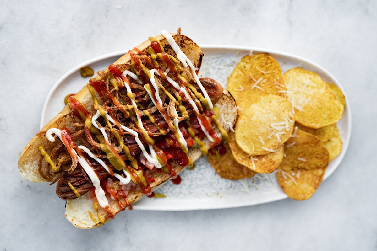 Loaded hot dog with various toppings served on a plate with potato chips