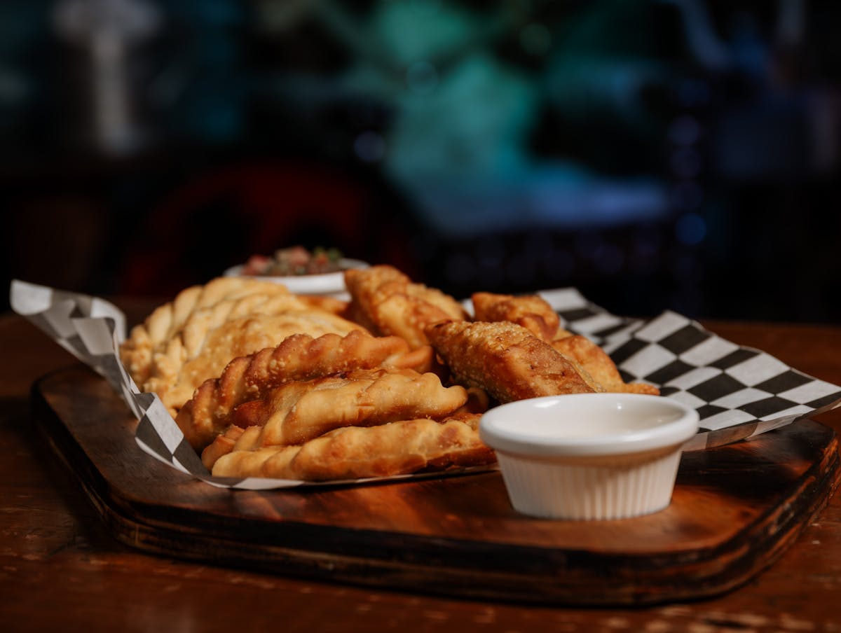 Freshly made empanadas arranged on a wooden tray with dipping sauce