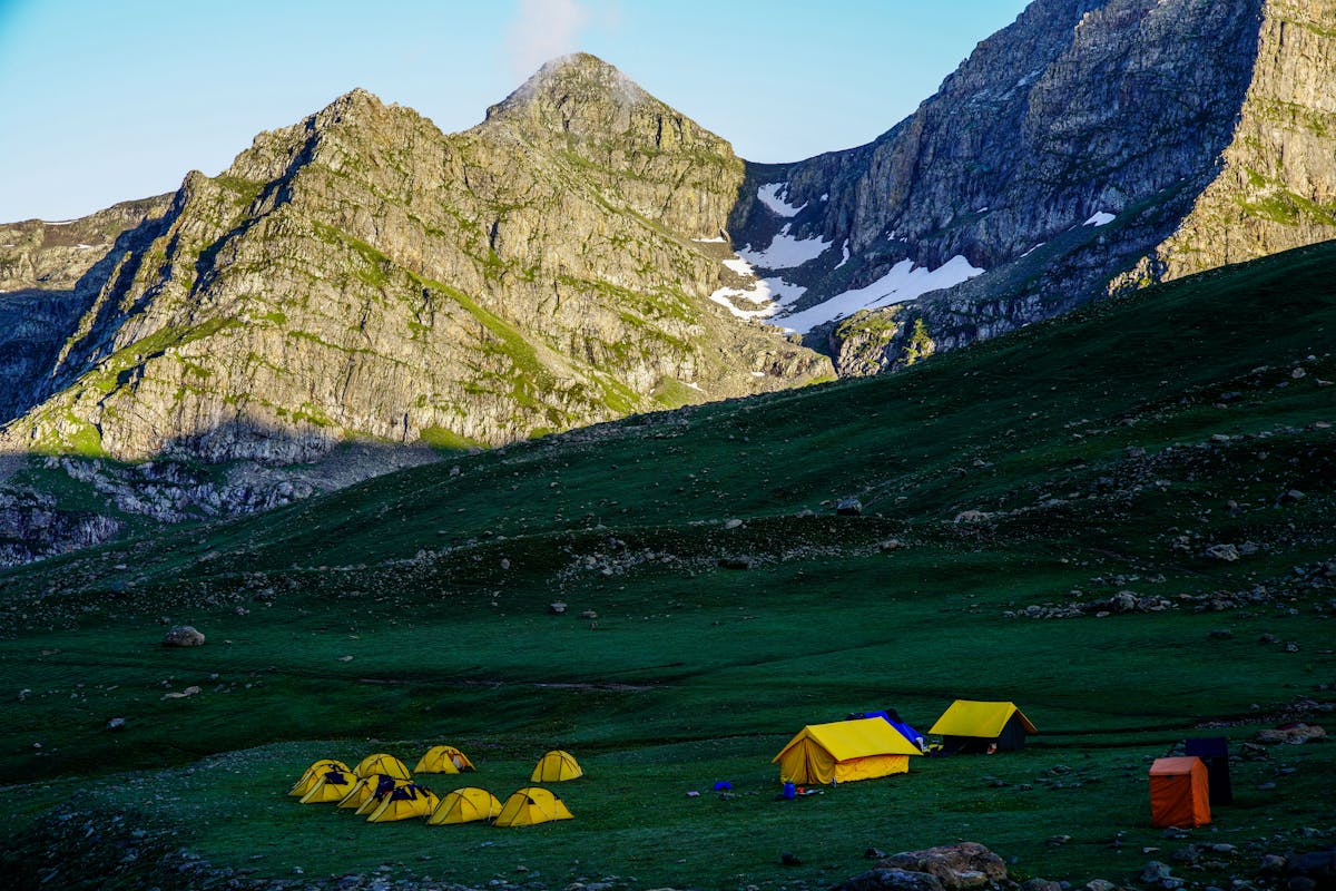 Yellow tents pitched in a mountain valley at sunrise with dramatic peaks behind