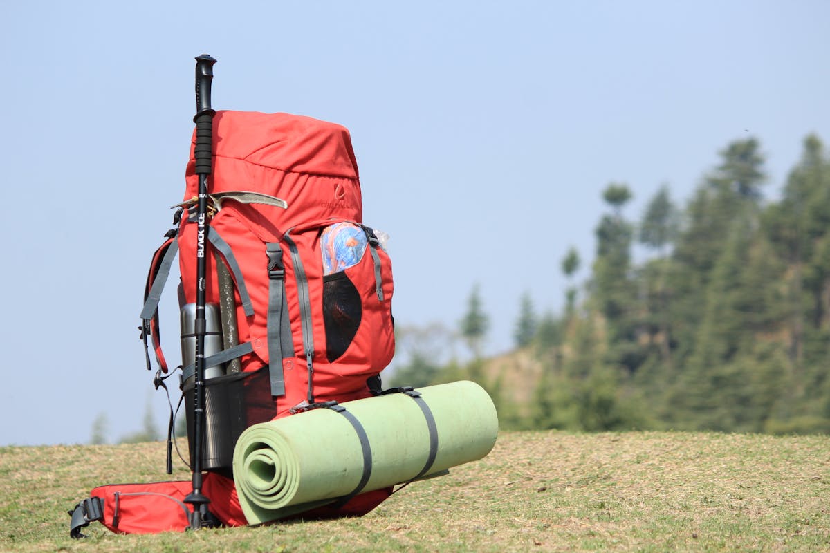 Red hiking backpack with trekking poles and gear on a grassy field