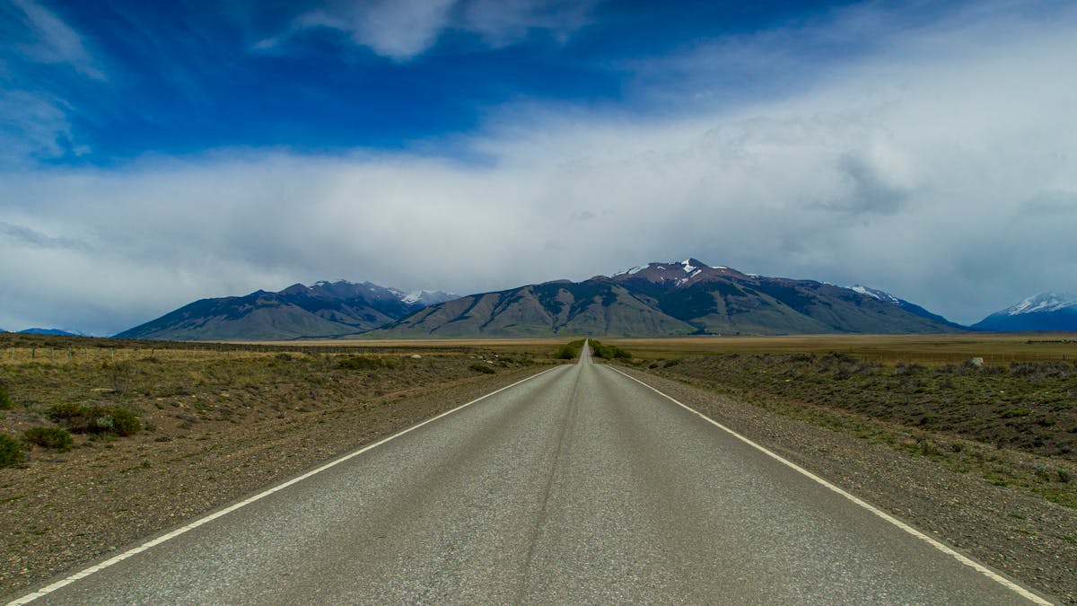 Straight road cutting through Patagonian steppe toward Andes mountains under dramatic sky