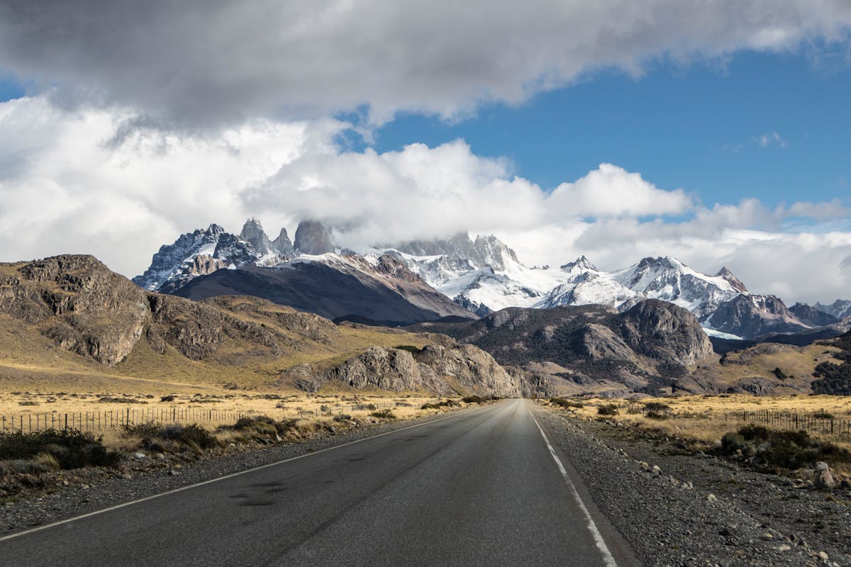 Highway stretching toward snow-covered mountains under dramatic stormy sky in Patagonia