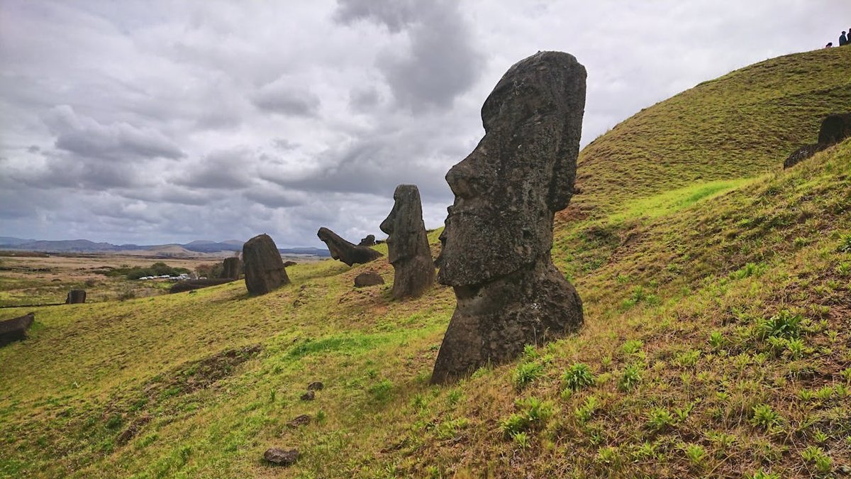Moai statues standing on a lush green hillside on Easter Island under dramatic cloudy sky