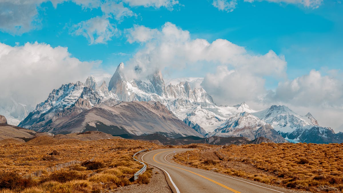 Long road stretching toward Mount Fitz Roy in Patagonia with green grassland on either side