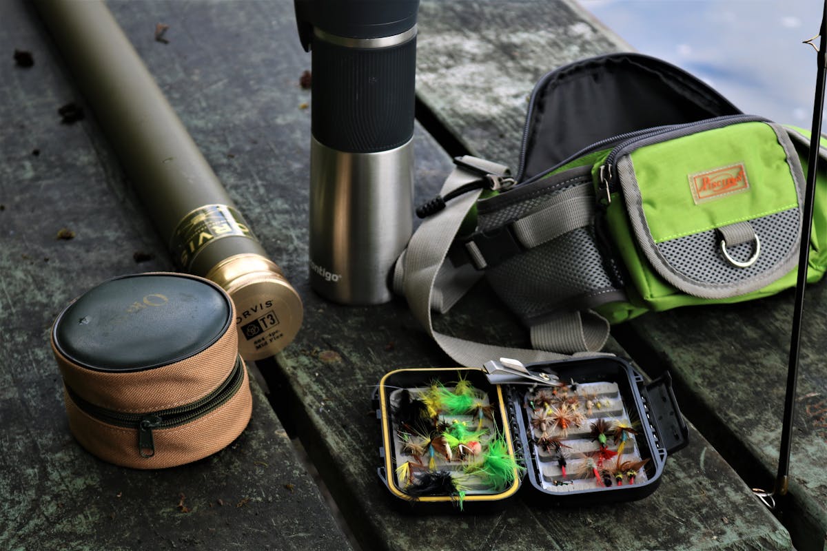 Fly fishing equipment laid out including fly box, rod, reel, backpack and accessories
