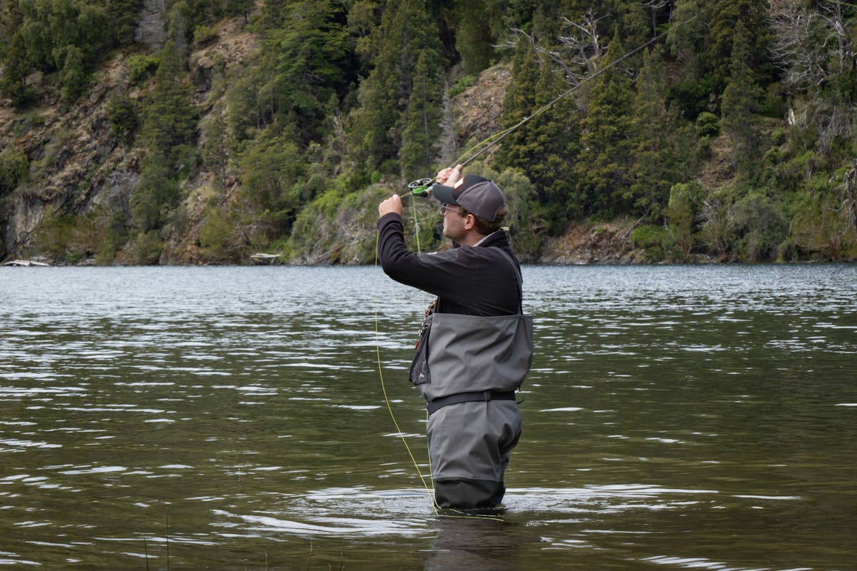 Man fly fishing in a clear river surrounded by Patagonian forest and mountains