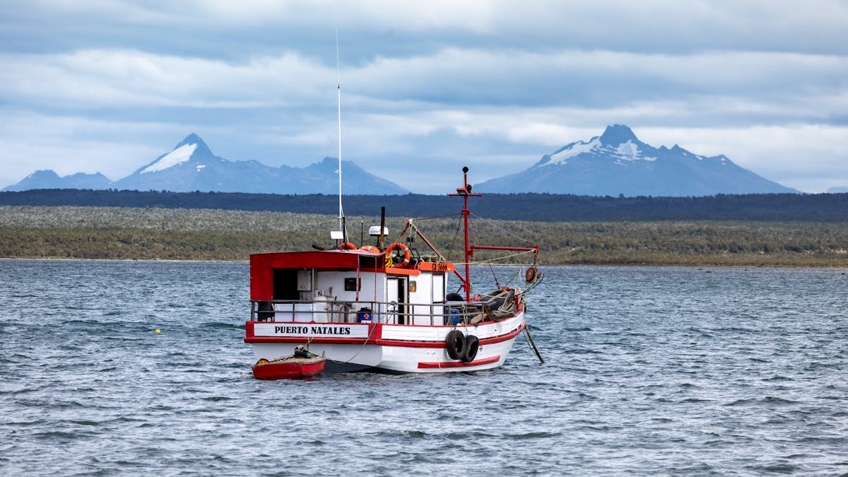 Wooden fishing boat on calm waters with mountains in the background at Puerto Natales Chile