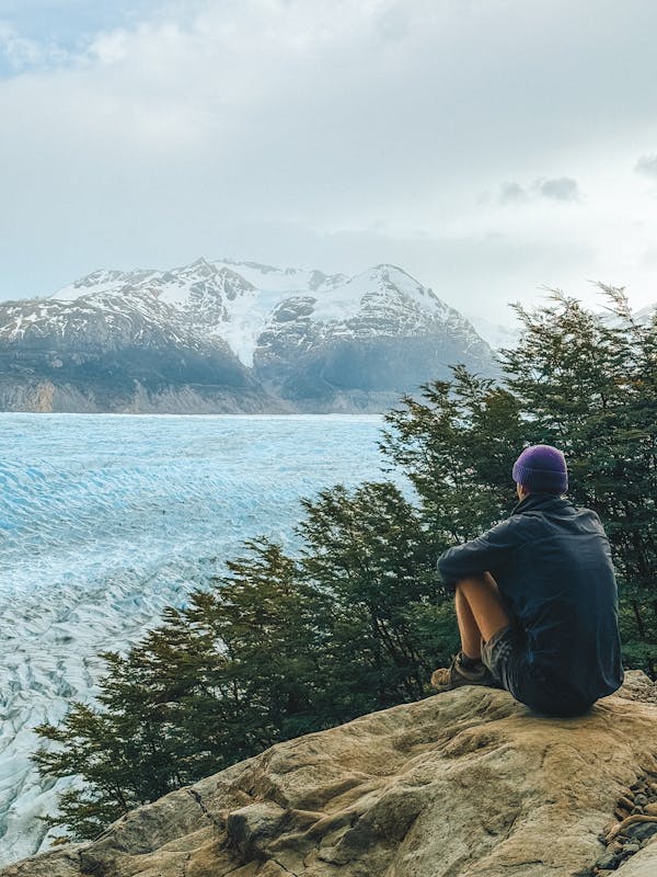 Hiker sitting on rock overlooking Grey Glacier and mountain range in Chilean Patagonia