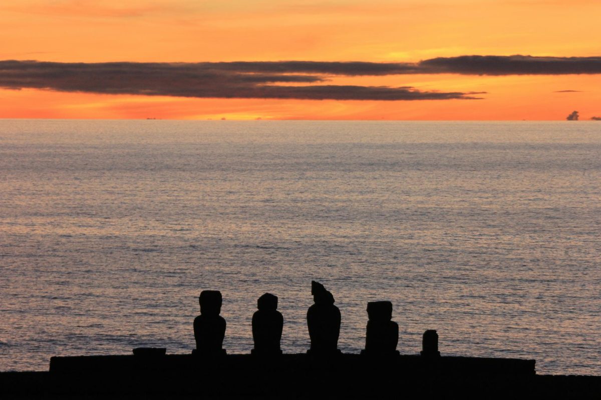 Moai statues silhouetted against a colorful sunset on Easter Island, Chile