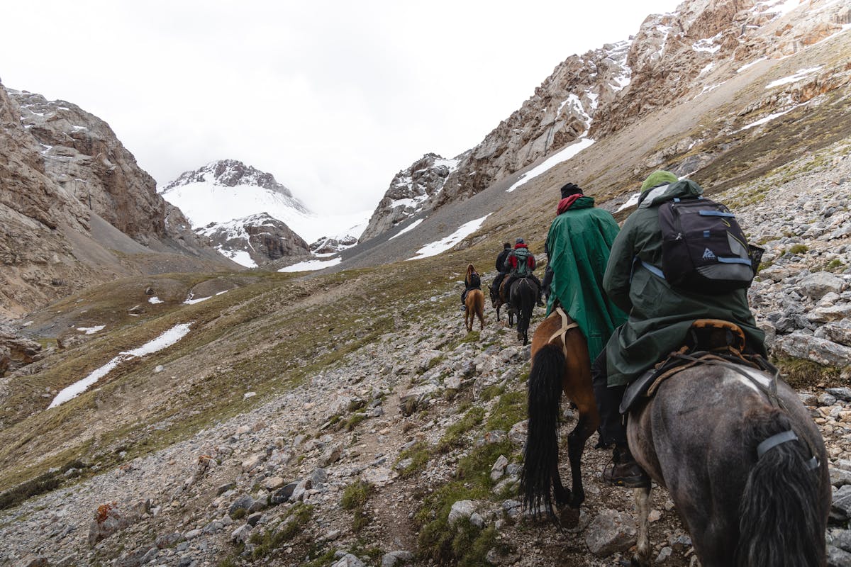 Group of horseback riders making their way through rugged snowy mountain terrain