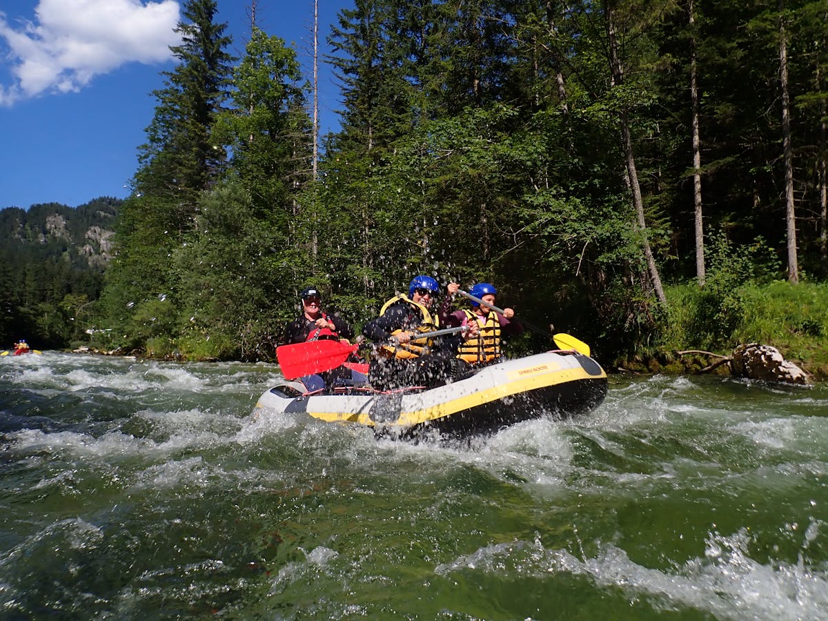 Group of adventurers whitewater rafting through a forested river