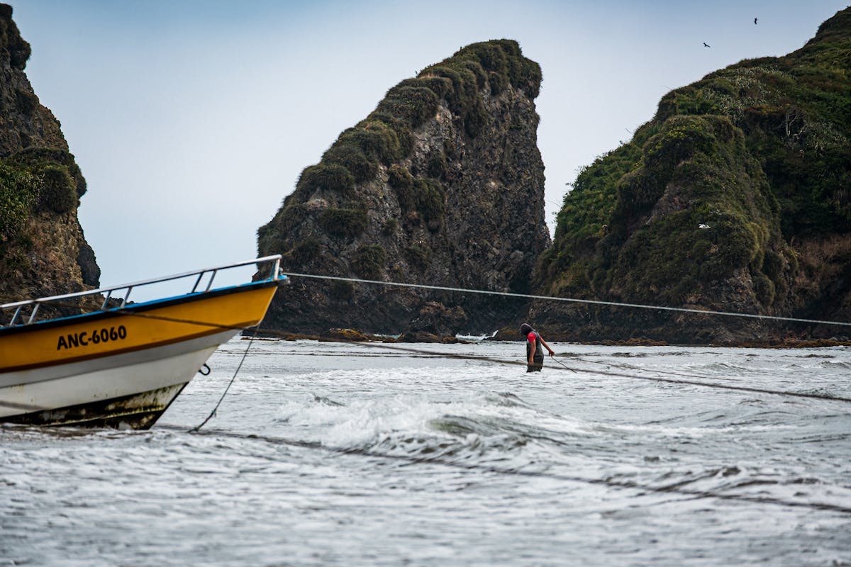Fishing boat and fisherman near rocky coastal cliffs in Ancud, Chiloe