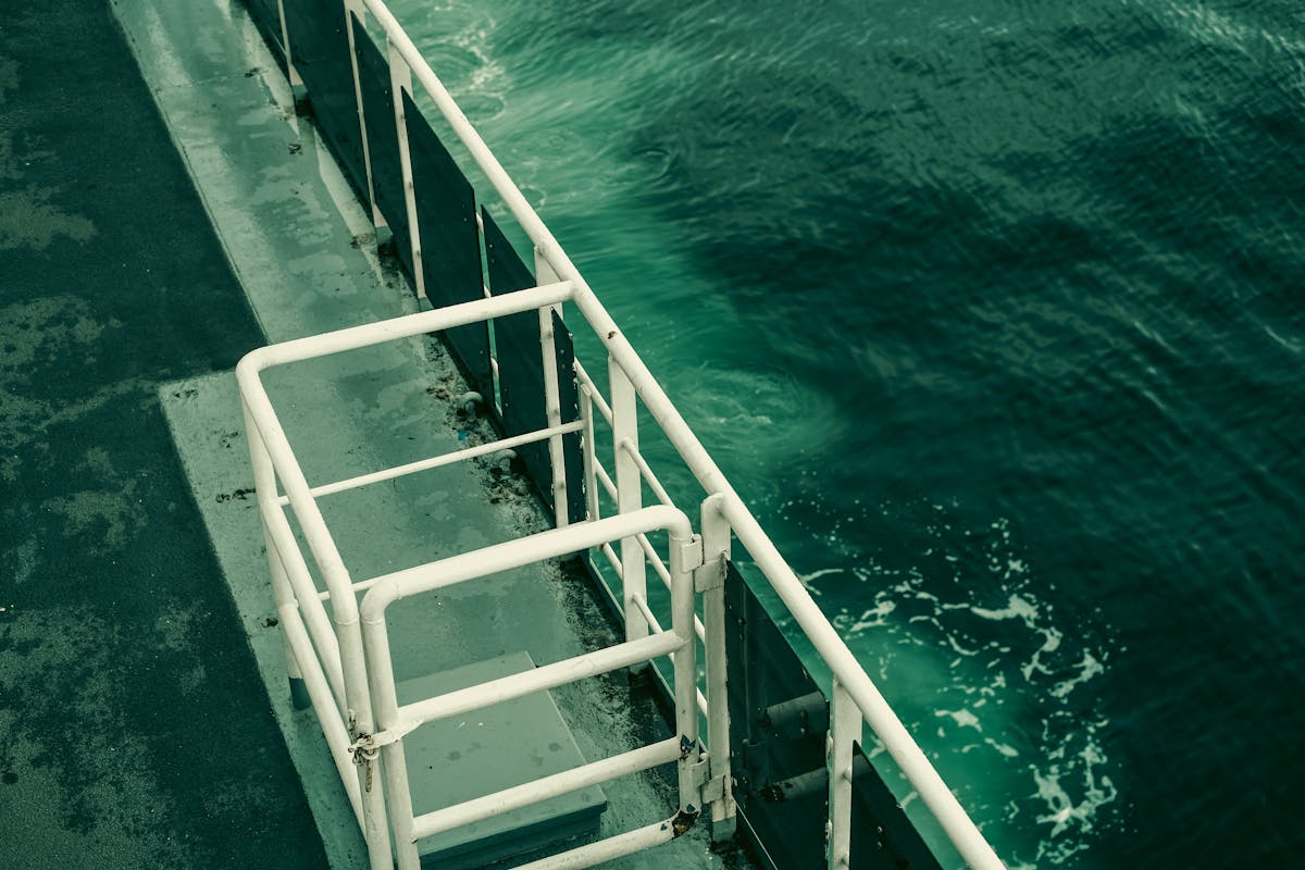 Ship deck with metal railing over green ocean water on a calm day
