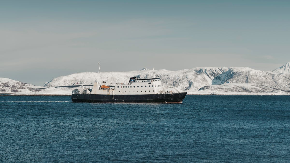 A ferry navigating through a fjord with snow-covered mountains in the background