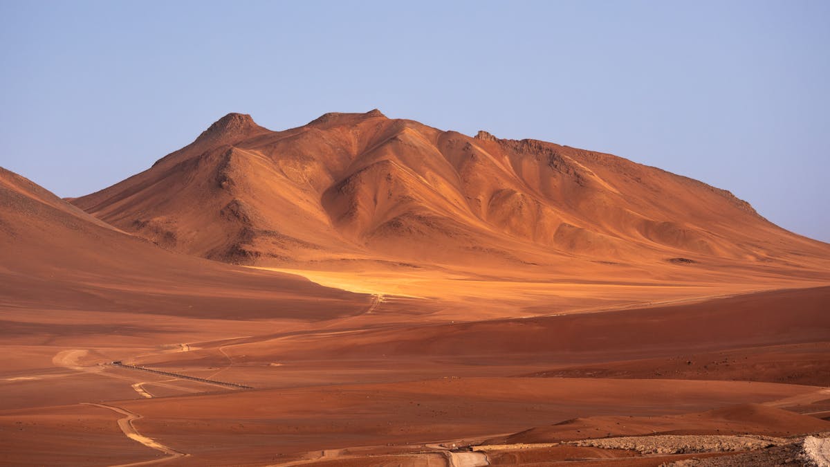 Rolling sand dunes in the Atacama Desert under clear blue sky with mountains in the distance