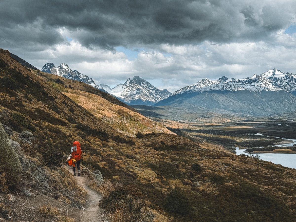Solo hiker trekking through mountains in Magallanes Chile with lake and peaks in background