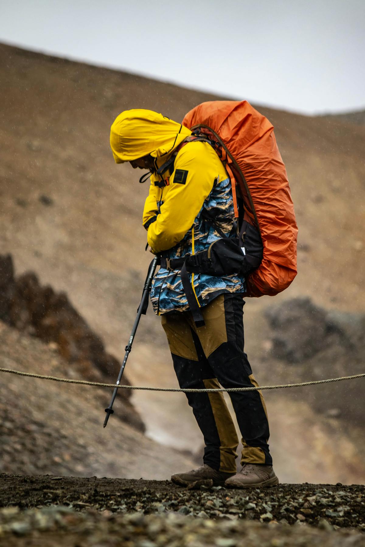 A hiker in colorful rain gear trekking through rugged terrain