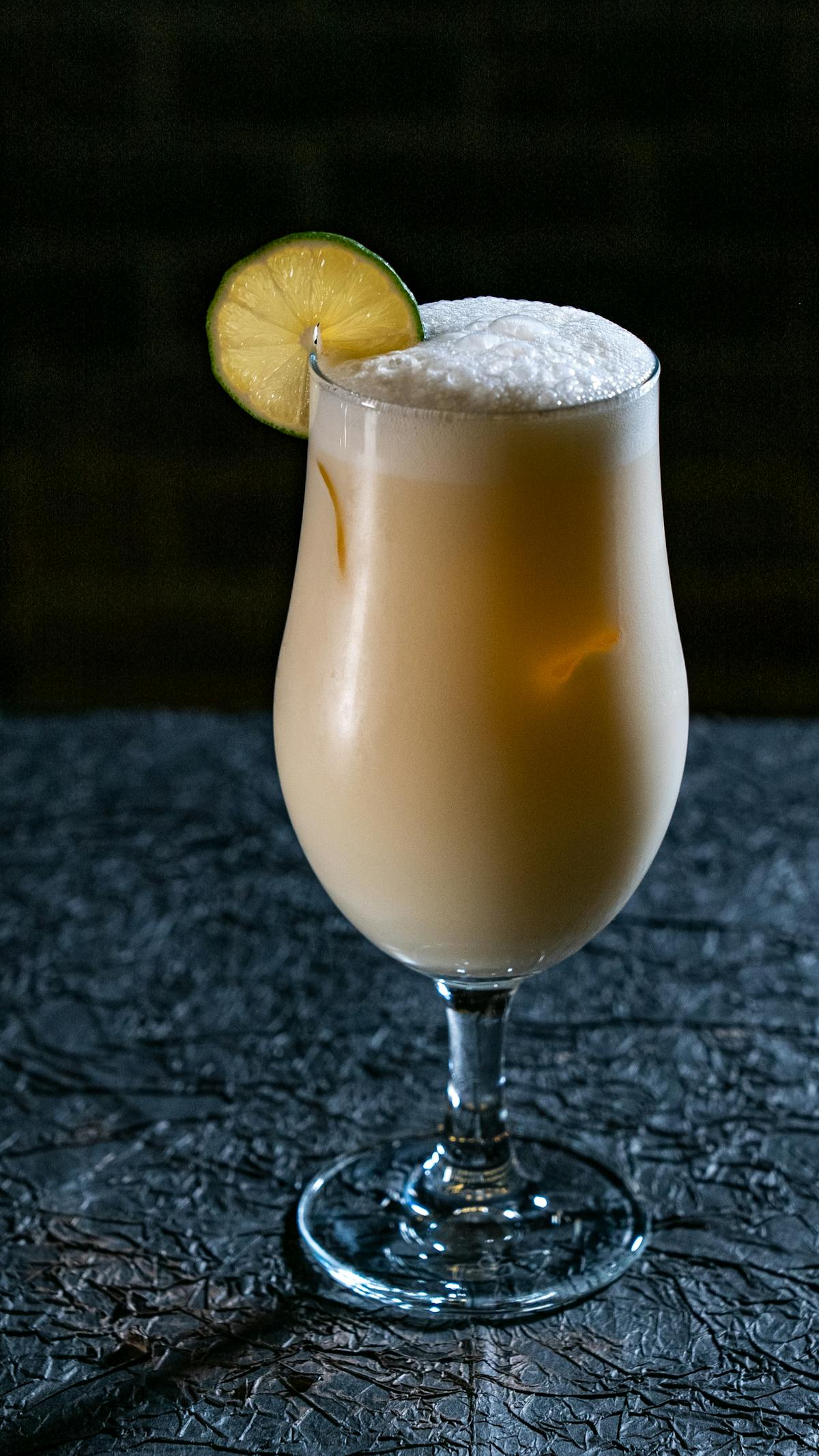 A frothy, creamy cocktail garnished with a lime slice on a textured surface
