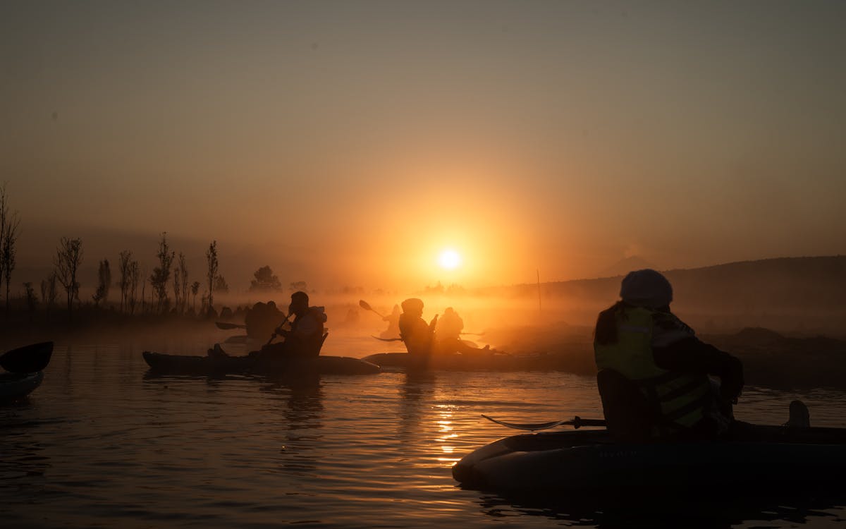Kayakers paddling through morning mist on a tranquil lake at sunrise