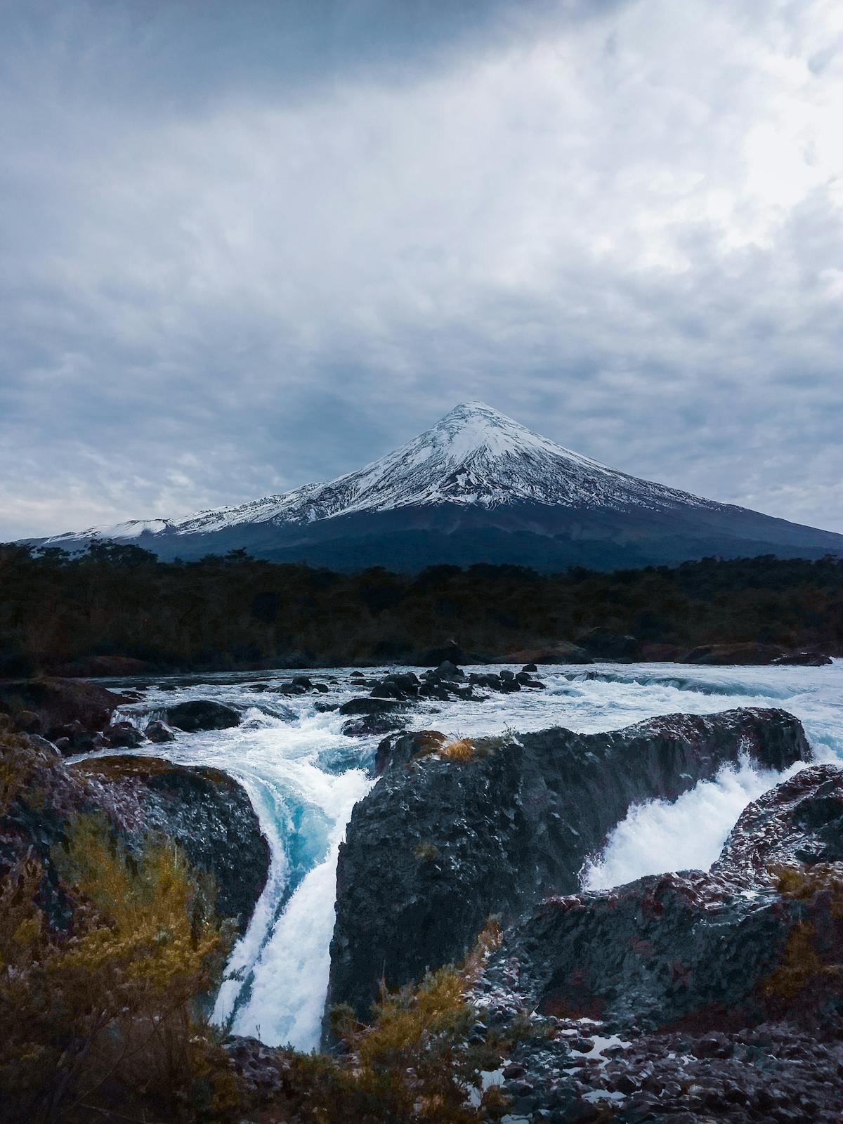 Rapids flowing past volcanic rock with a snow-capped volcano in the background