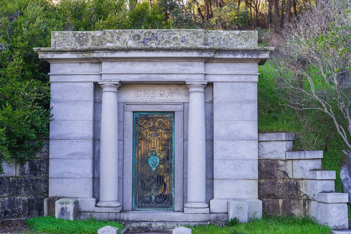 Ornate stone mausoleum with classical columns and decorative door in a historic cemetery