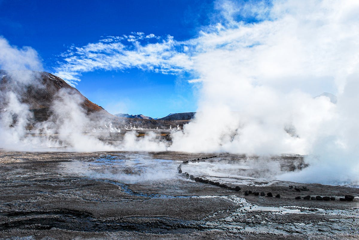 Steam rising from El Tatio geothermal field in Chile with clear sky and mountain backdrop