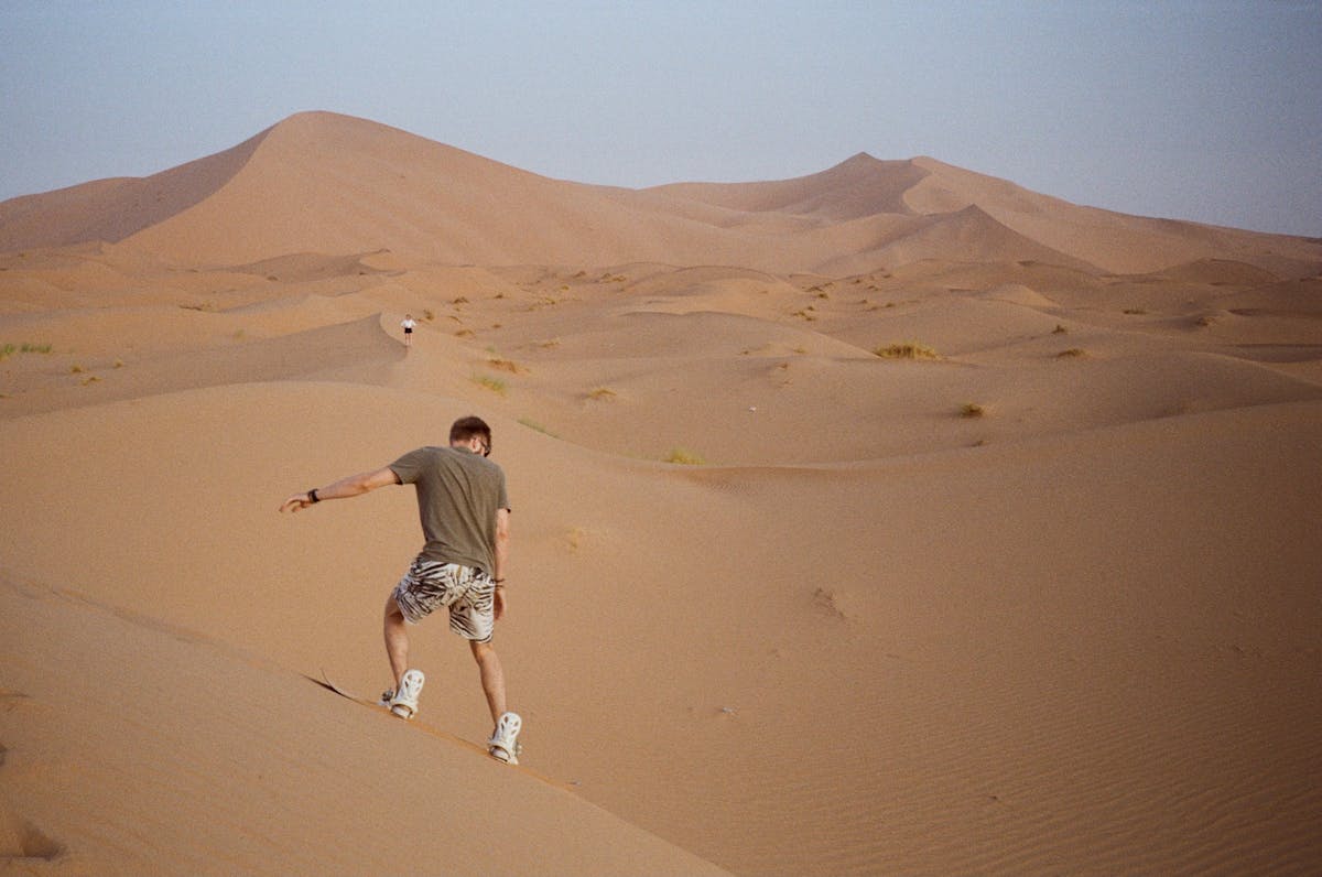 Person sandboarding down steep desert dunes at twilight