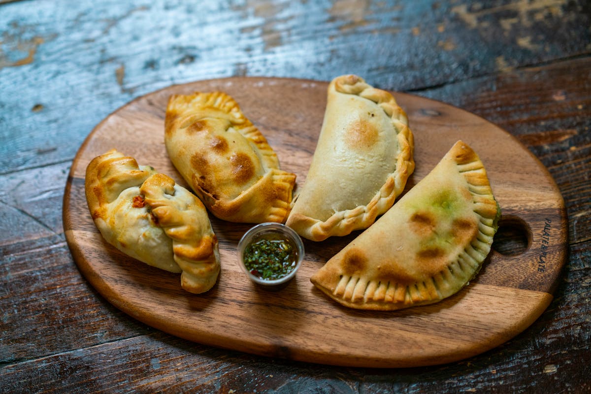Freshly baked empanadas served with dipping sauce on a wooden board