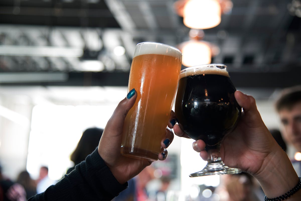 Two hands clinking glasses of different craft beers in a modern bar setting