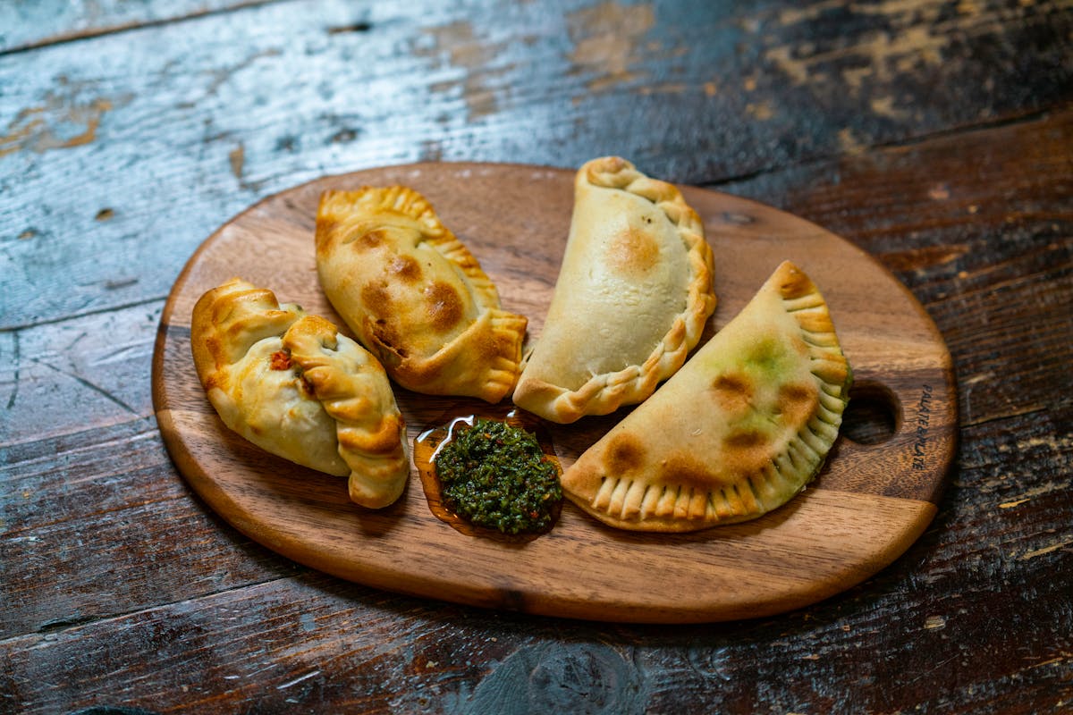 Baked empanadas with chimichurri sauce served on a rustic wooden board