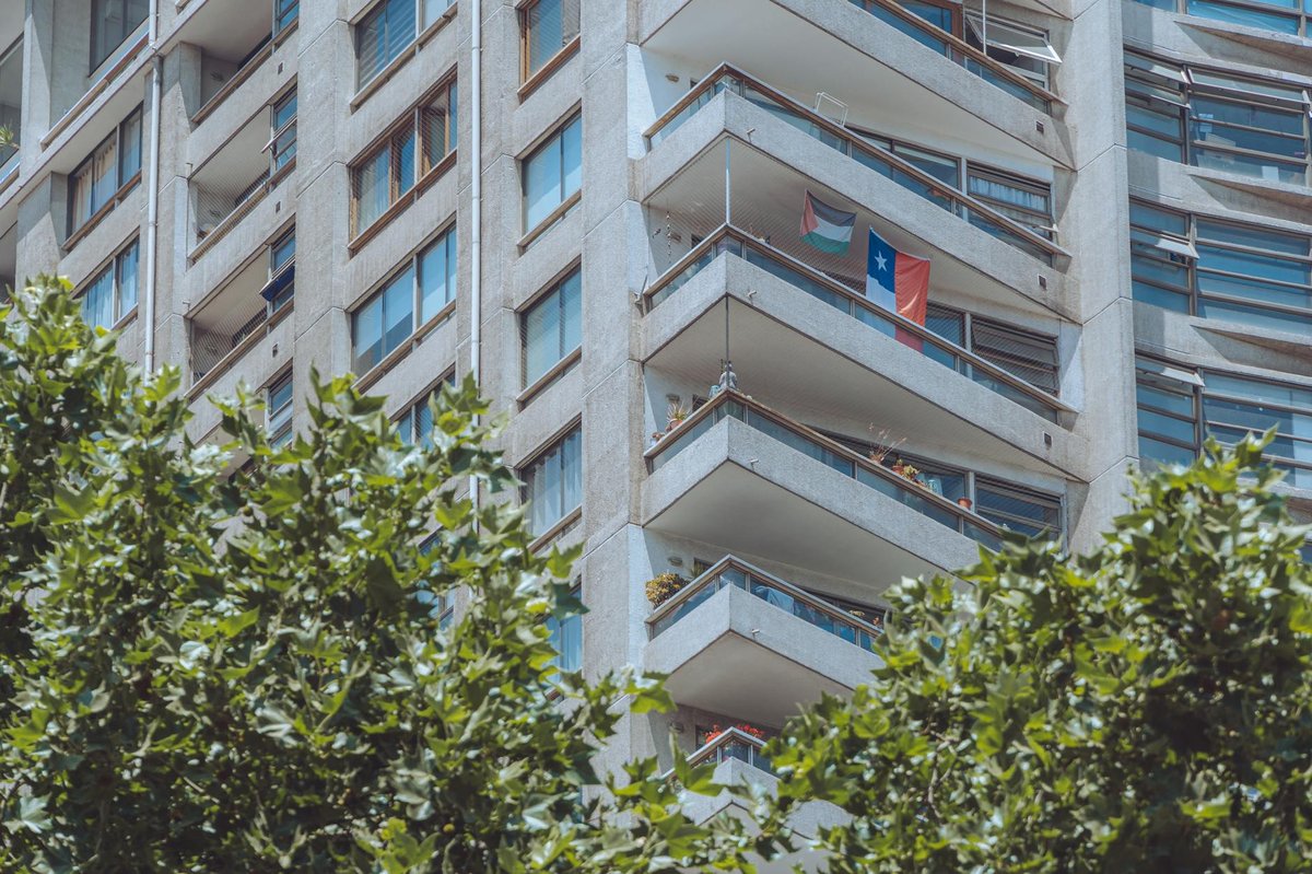 Modern apartment building in Santiago with a Chilean flag on the balcony surrounded by trees