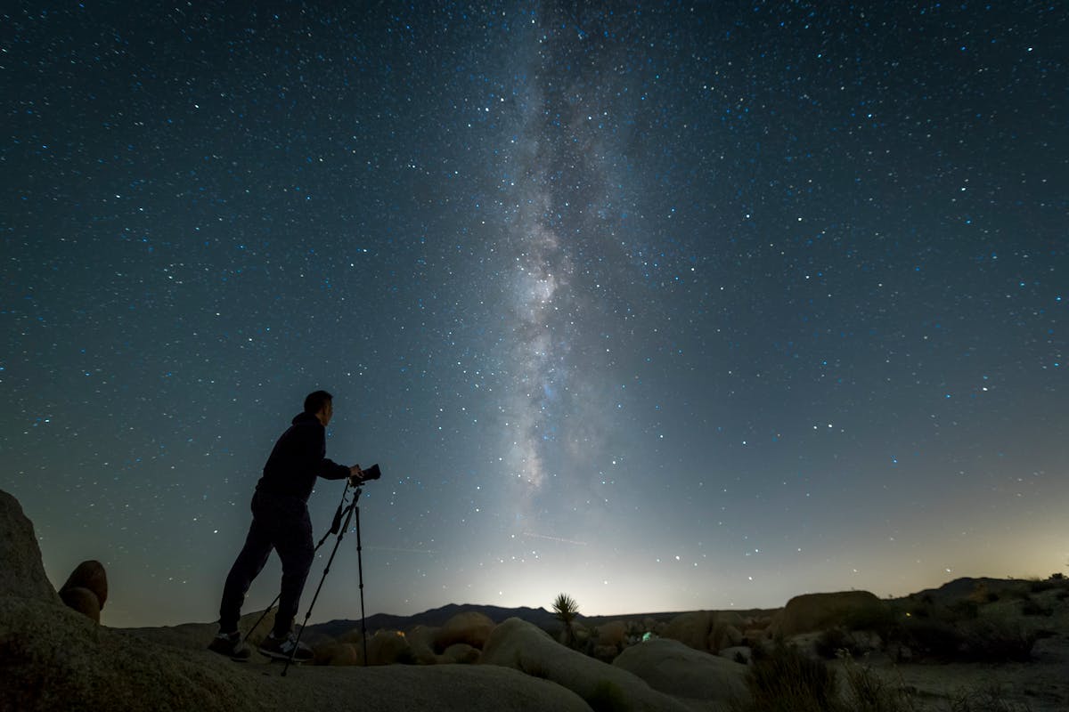 Photographer with camera on tripod capturing the Milky Way in a dark desert landscape at night