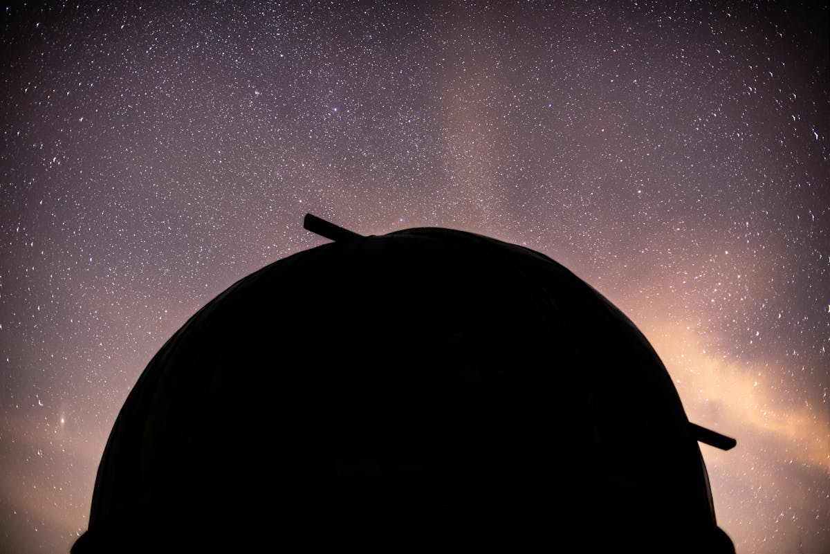 Silhouette of an observatory dome against a dramatic starry night sky