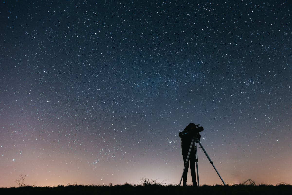 Silhouette of a person using a telescope to observe the night sky filled with stars