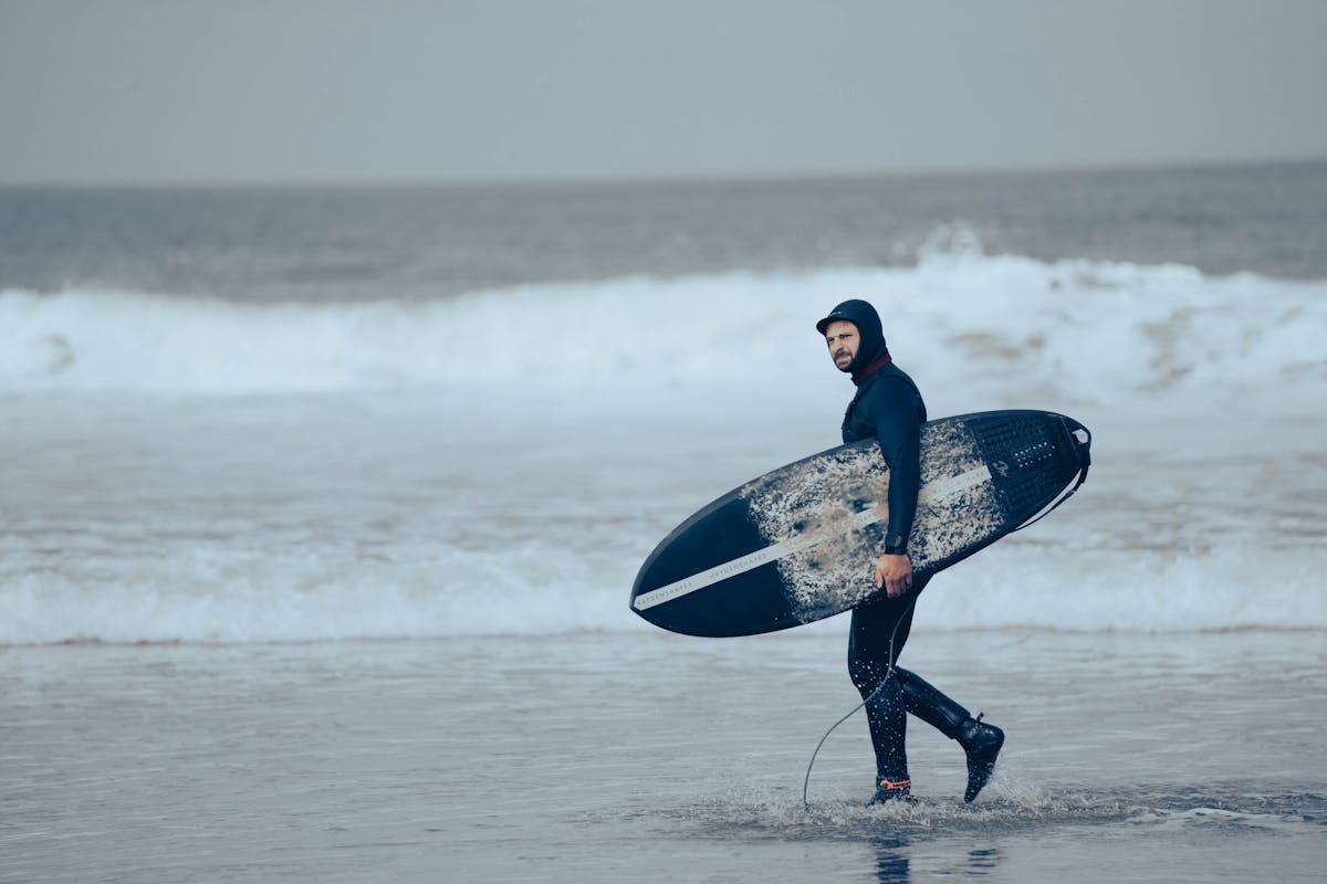 Man in wetsuit standing by the ocean holding a surfboard, ready to surf
