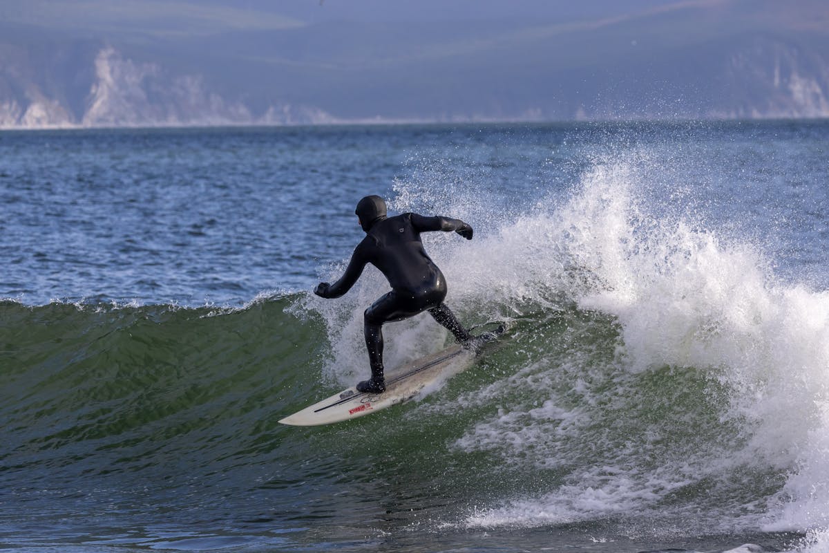 Surfer wearing a full wetsuit riding a wave in cold ocean water