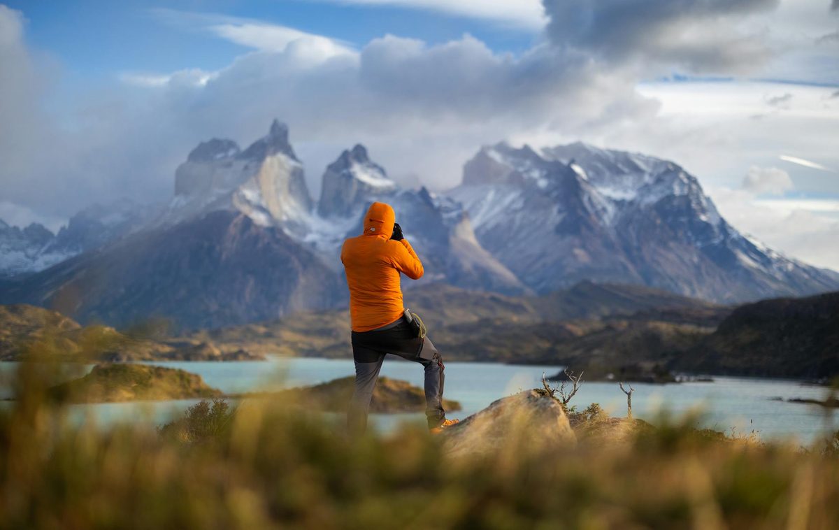 Hiker in orange jacket standing before Torres del Paine peaks at sunrise