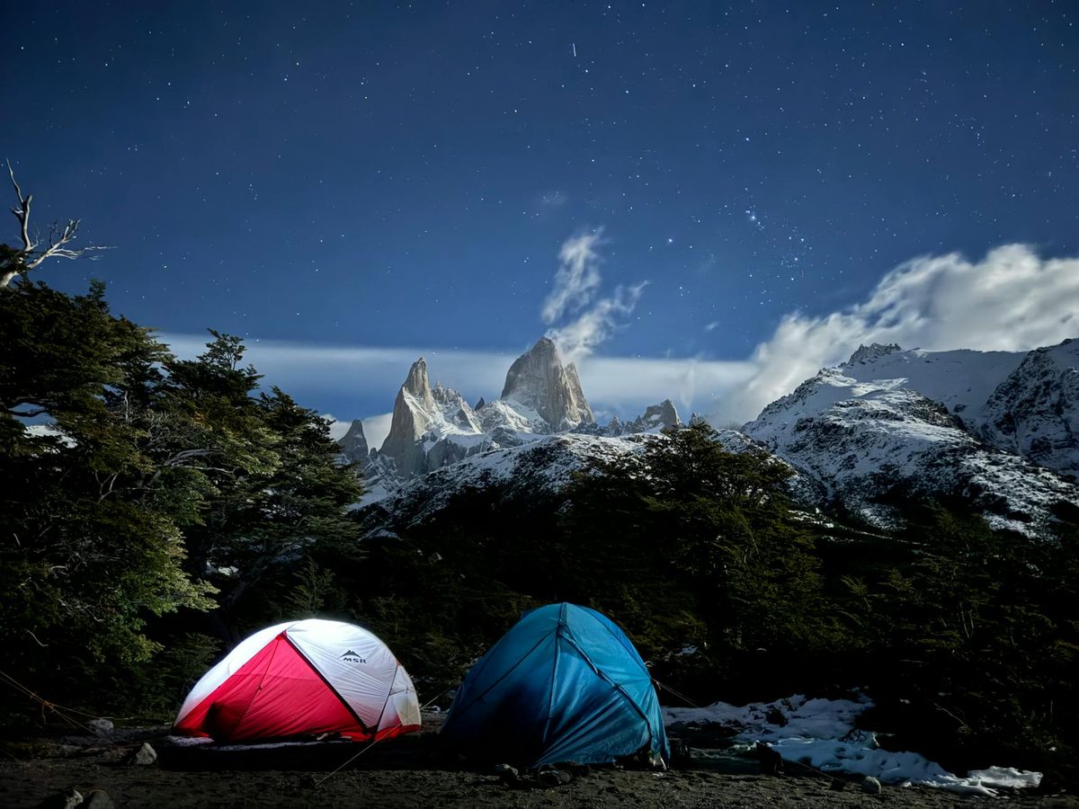 Camping tents illuminated at night with mountain peaks and starry sky in Patagonia