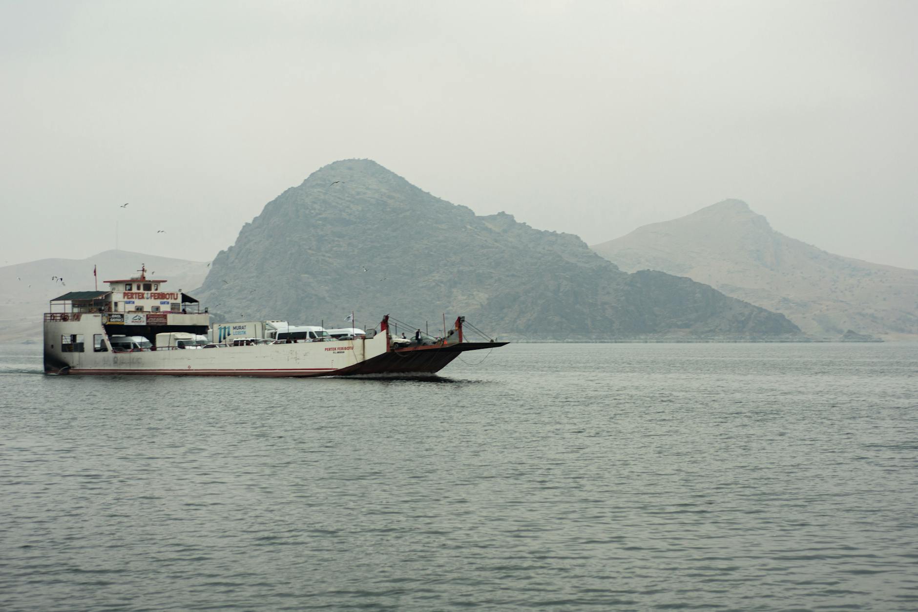Car ferry crossing calm waters with mountainous coastline in the background