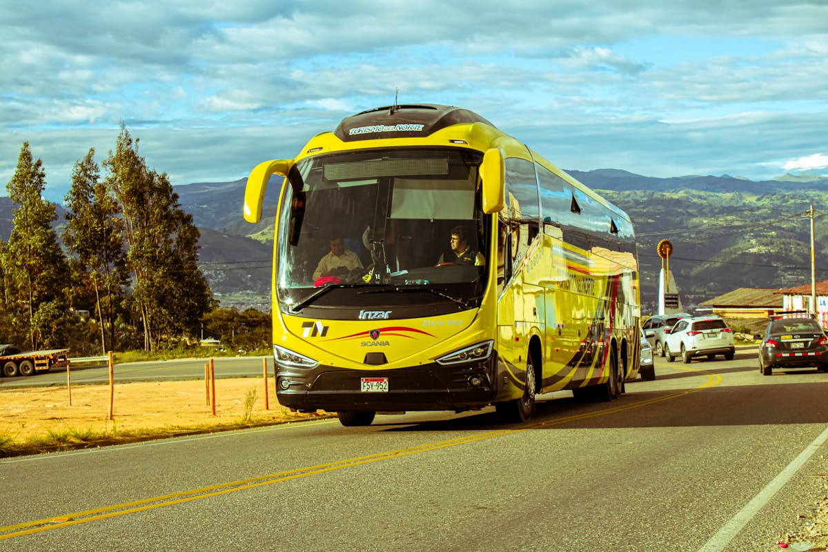 Yellow bus traveling on a scenic mountain road under a blue sky in Chile
